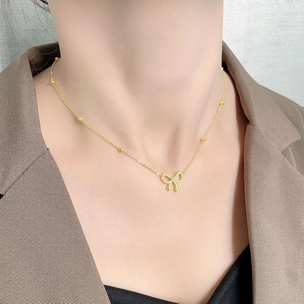 Gold-tone bow charm necklace worn as a delicate everyday necklace