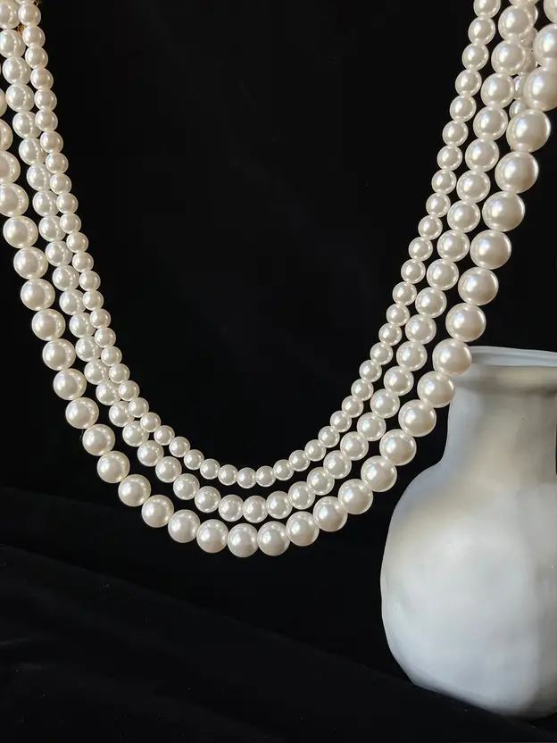 Layered white pearl necklace displayed on a black jewelry stand